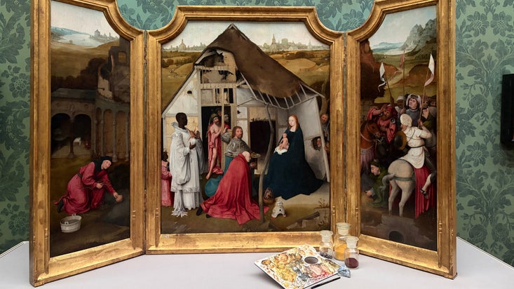 A painting showing a religious scene with a gold frame and differnrent colour paints in front